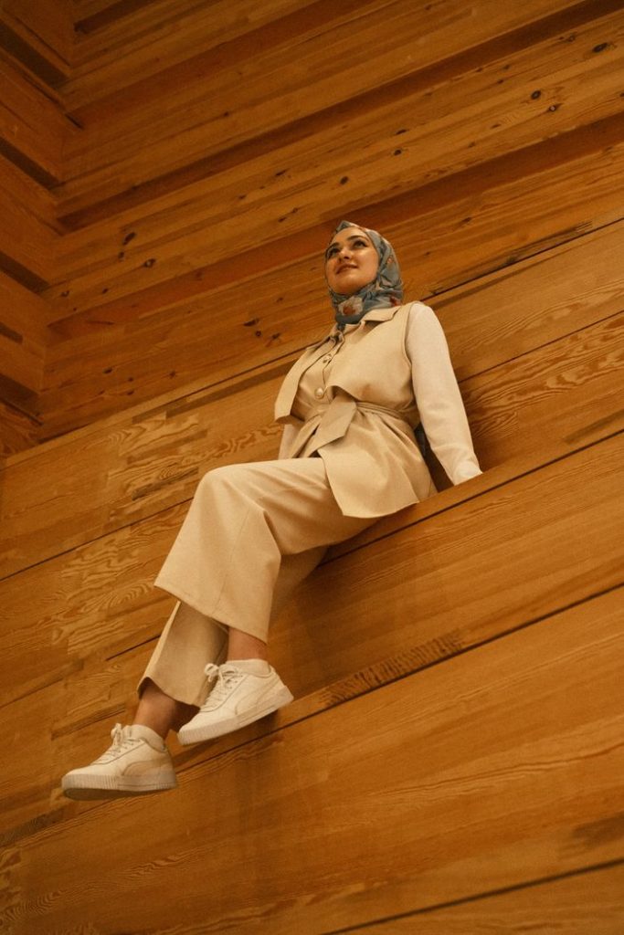 Fashionable woman in a hijab sitting elegantly on a wooden wall, showcasing modern style and confidence.