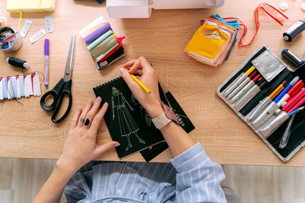 Designer sketching fashion outfits in a vibrant workshop with colorful fabrics and tools.
